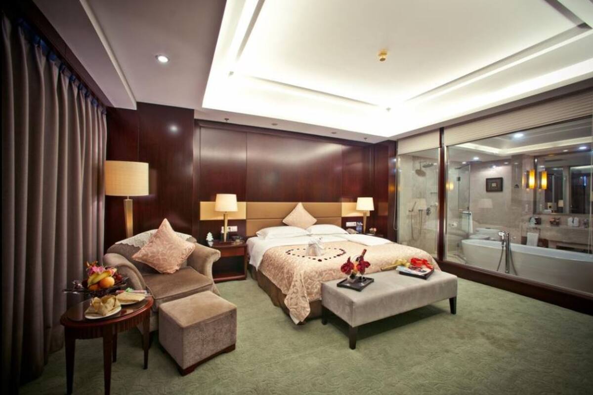 A hotel room with a large bed, a sofa, a small table with fruit, and a view of the bathroom.