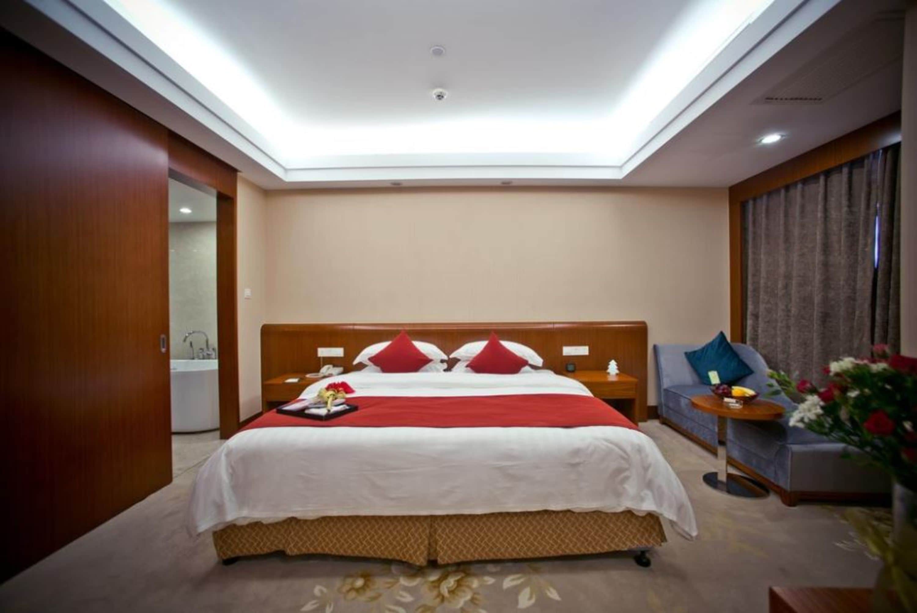 Habitación de hotel con una cama grande, un sofá, una mesita y un baño visible a través de una puerta abierta.