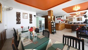 A dining area with a glass table, chairs, and a chandelier. There is a kitchen in the background with a refrigerator and a sink. - OYO 126 Patong Station House (Patong)