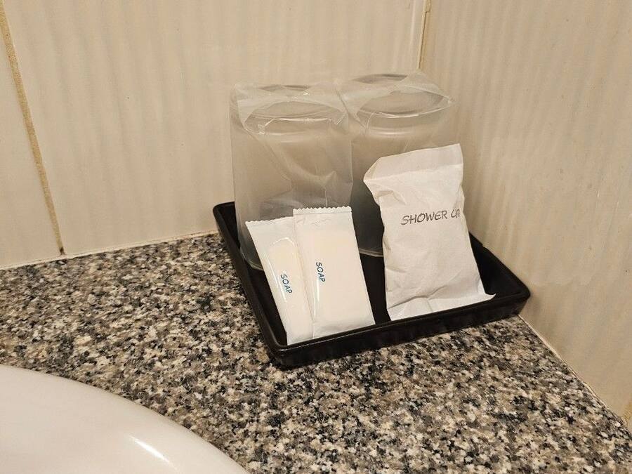 A bathroom counter with a sink, a tray holding two clear glasses, two soap packets, and a tissue.
