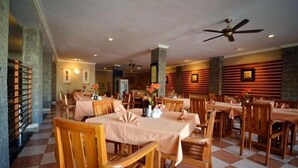 A spacious dining area with multiple tables and chairs, ceiling fans, and a checkered floor pattern. - Taman Rosani Hotel (Keroboken Kelod)