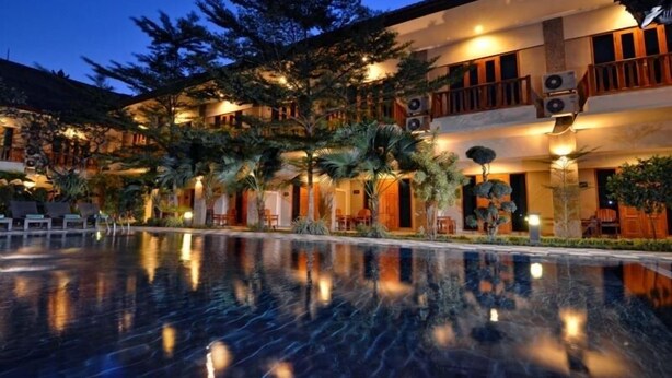 A hotel with a reflective pool, outdoor seating, and a well-lit facade at dusk. - Taman Rosani Hotel (Keroboken Kelod)