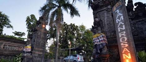 A stone entrance with a sign for the Tamanrosan Hotel, surrounded by palm trees and a parked car.