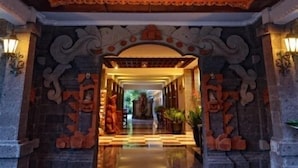 An ornate entrance with a wooden ceiling and a chandelier, leading to a corridor with stone carvings and potted plants. - Taman Rosani Hotel (Keroboken Kelod)