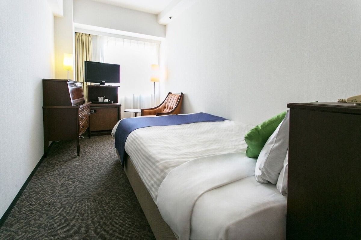 Hotellihuone, jossa on sänky, työpöytä, jossa on televisio, tuoli ja lipasto.