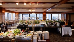 Un buffet proposant une variété de plats et de mets, un lustre et une vue sur la ville grâce à de grandes fenêtres.