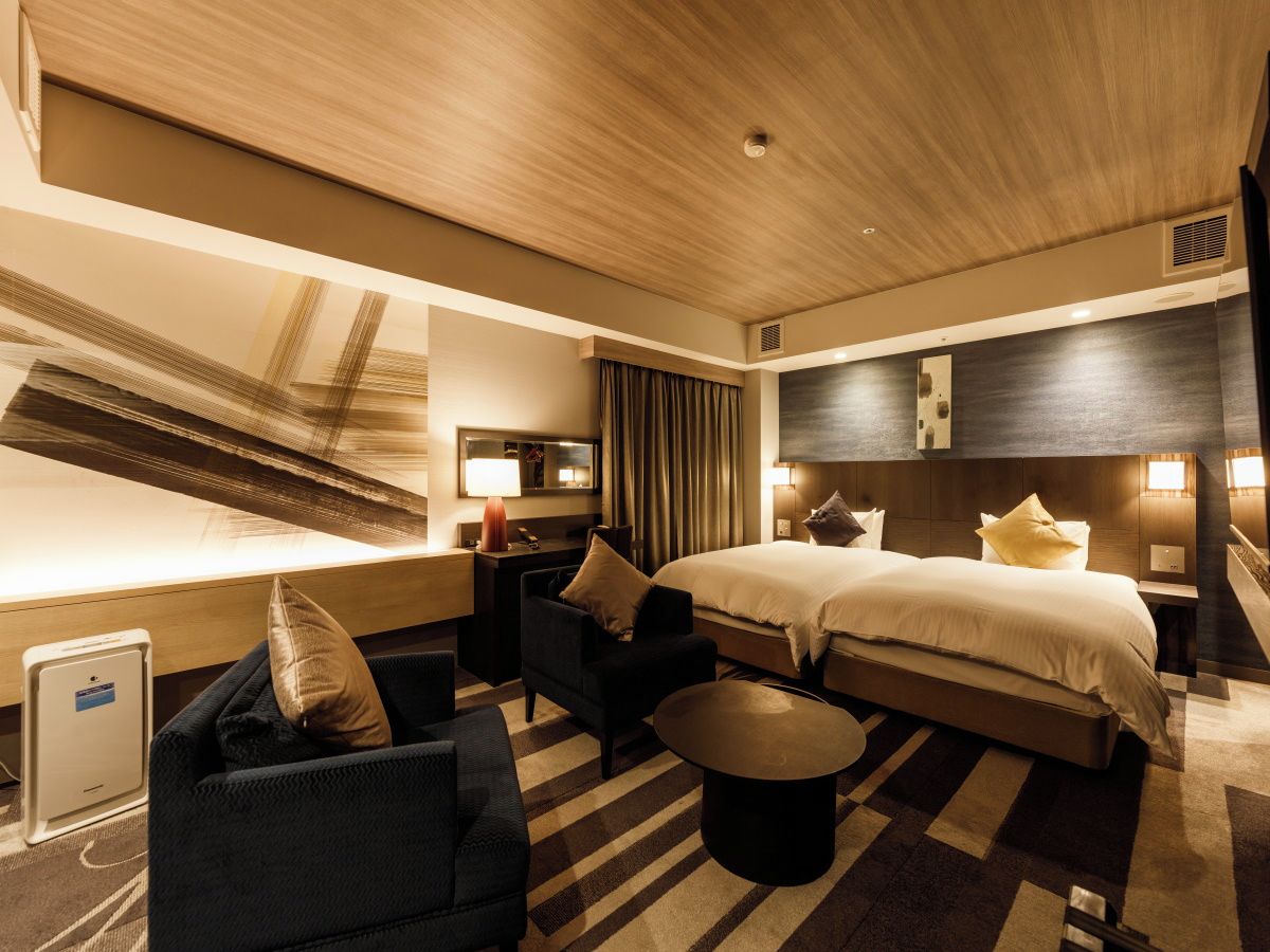 Quarto de hotel com uma cama grande, uma escrivaninha, uma cadeira e uma mesinha.