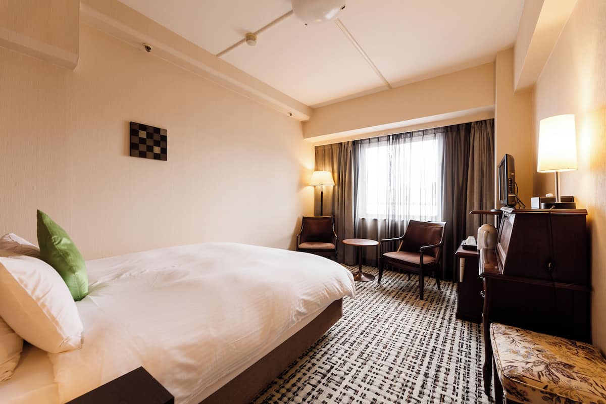 Hotellihuone, jossa on suuri sänky, työpöytä, kaksi tuolia, lamppu ja televisio.