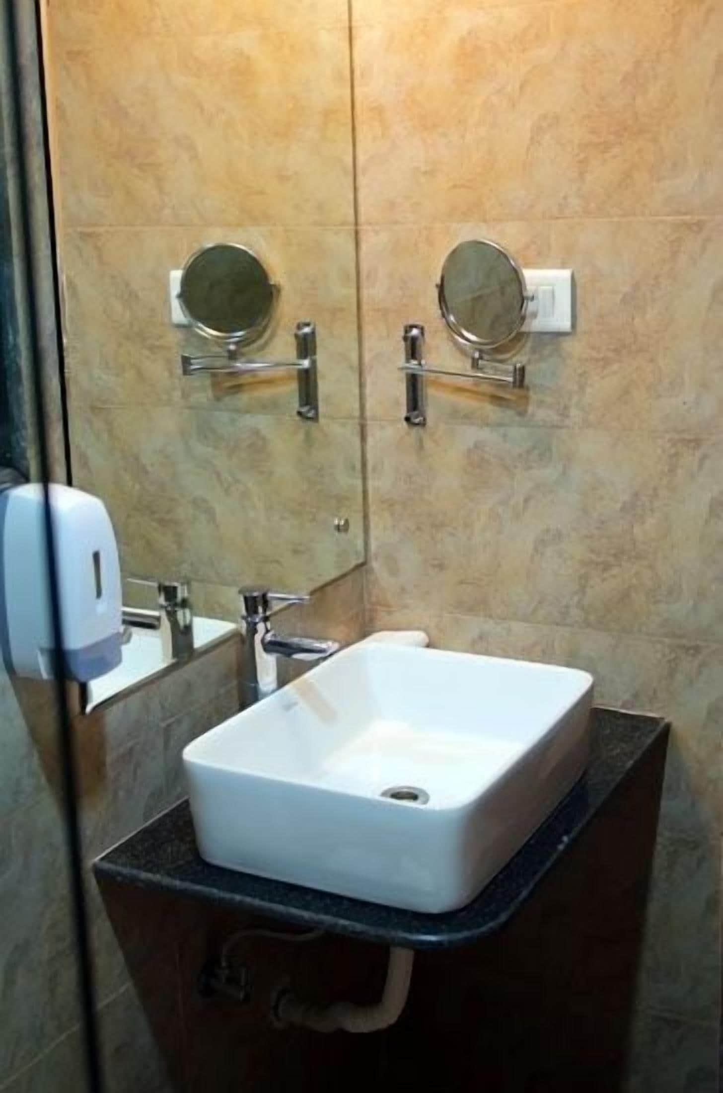 A bathroom with a white sink, two wall-mounted mirrors, and a soap dispenser.