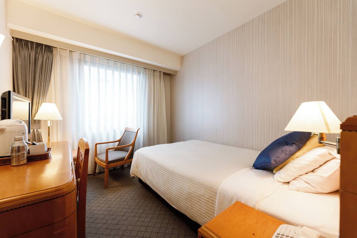 A hotel room with a bed, a desk with a lamp, a chair, and a telephone.