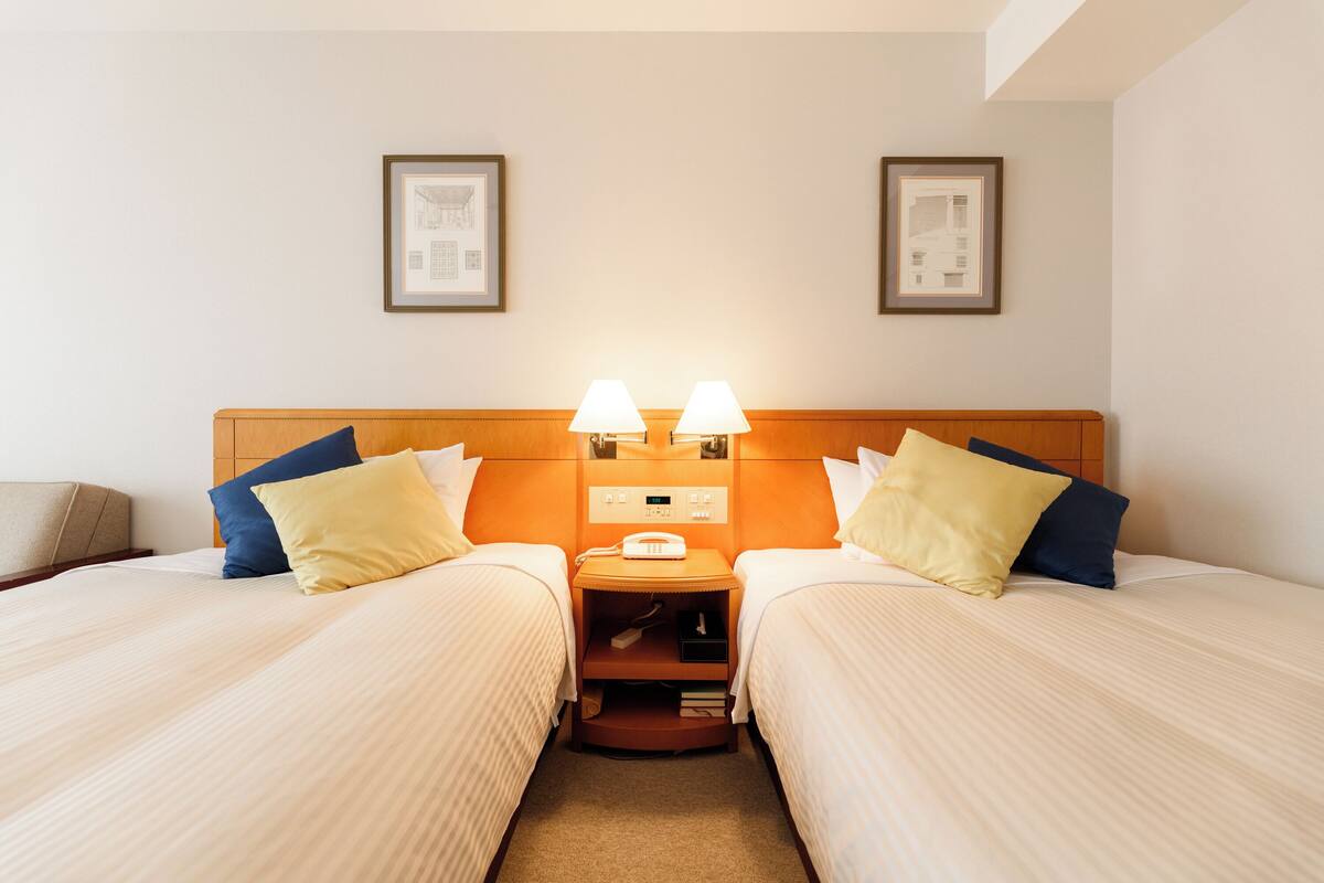 A hotel room with two beds, a nightstand with lamps, and framed pictures on the wall.