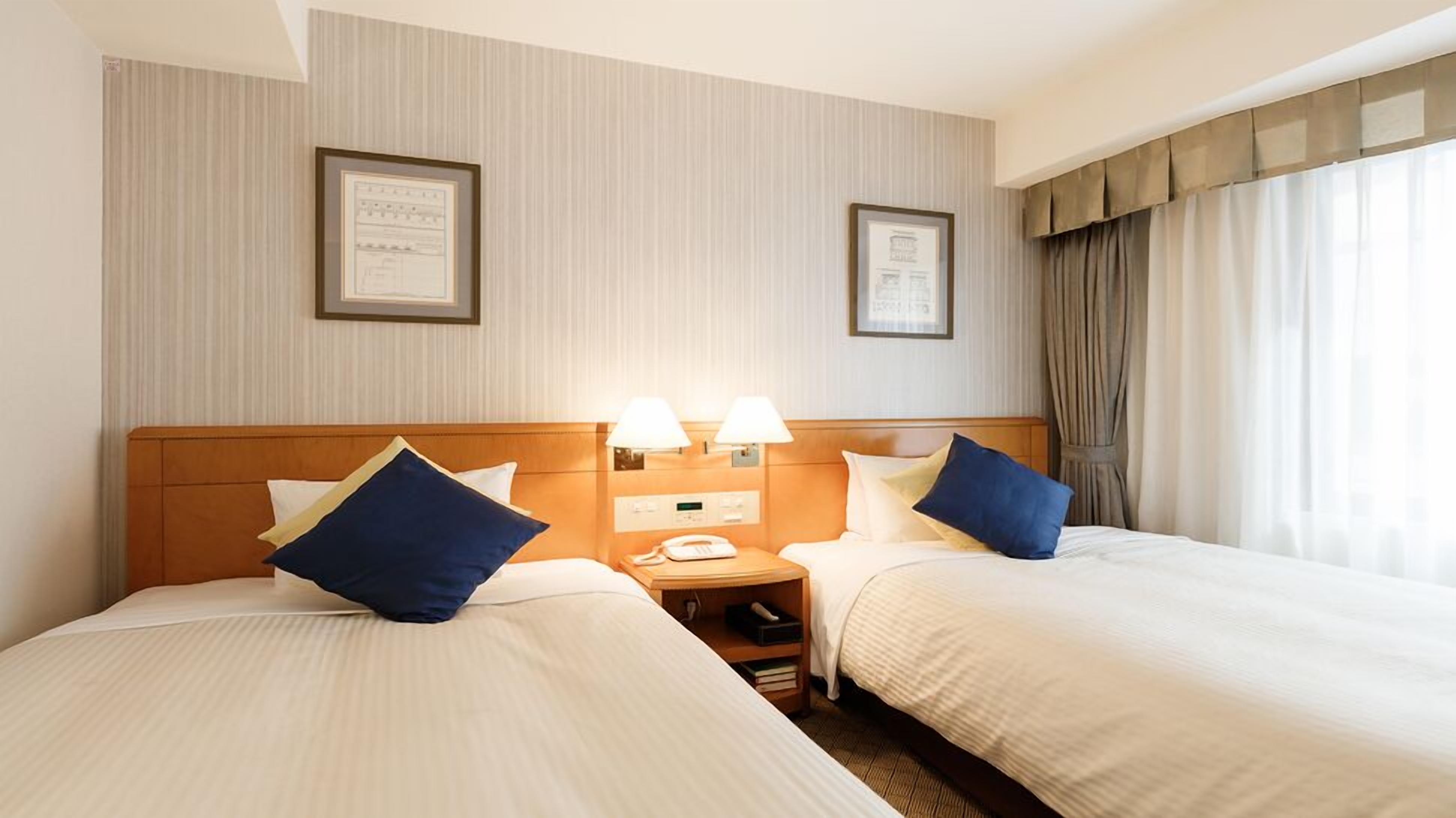 A hotel room with two beds, a bedside table with a phone, and framed certificates on the wall.