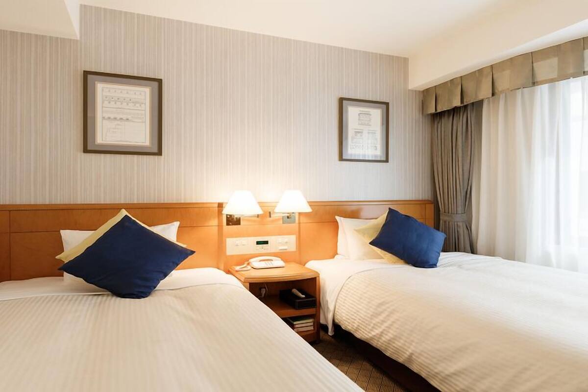 A hotel room with two beds, a bedside table with a phone, and framed certificates on the wall.