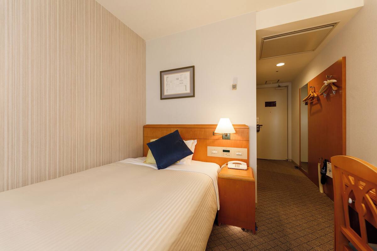 A hotel room with a bed, bedside table, lamp, and a framed picture on the wall.