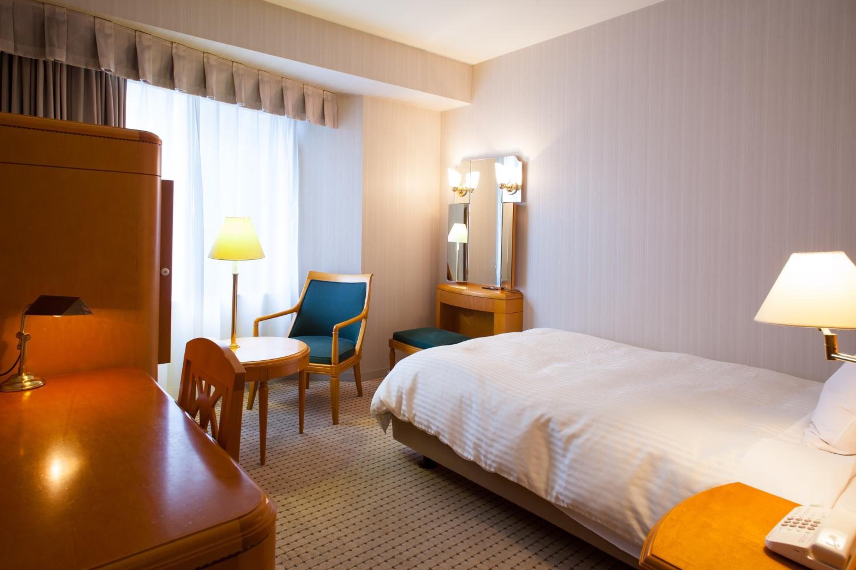 A hotel room with a bed, a desk, a chair, a lamp, and a mirror.