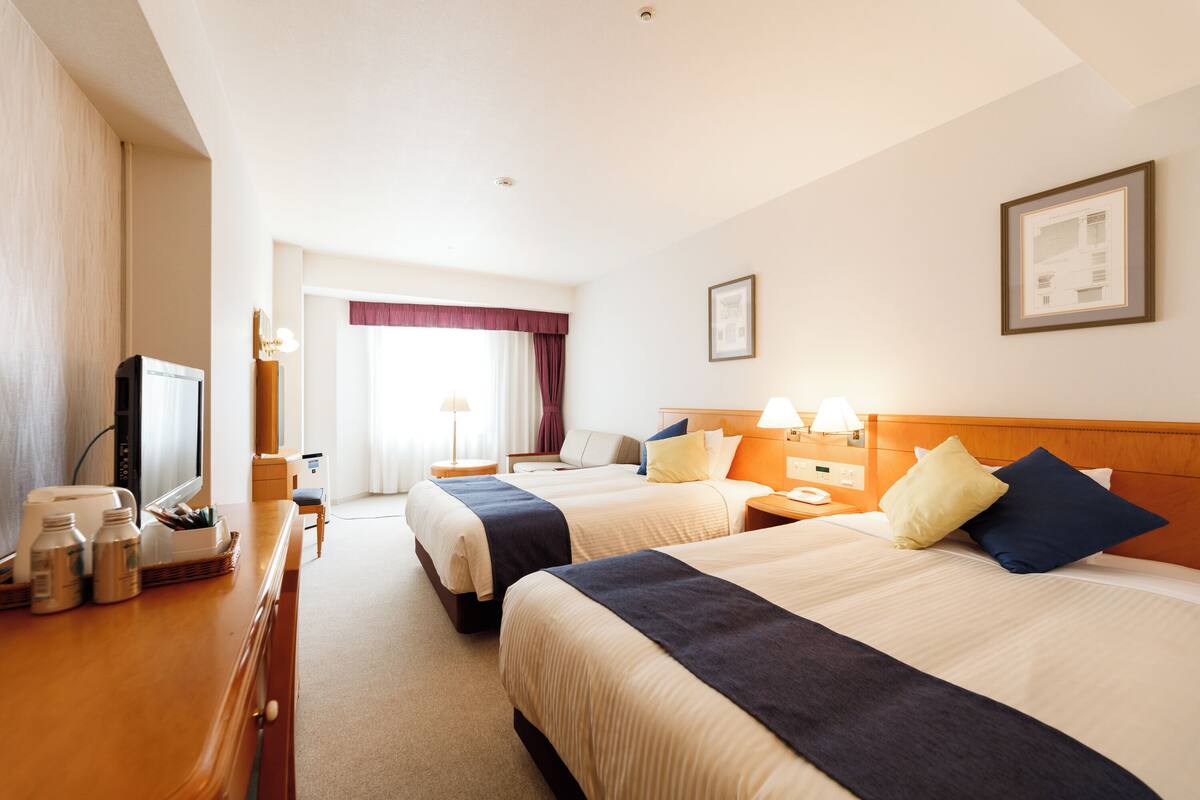 A hotel room with two beds, a desk with a television, and a window with curtains.