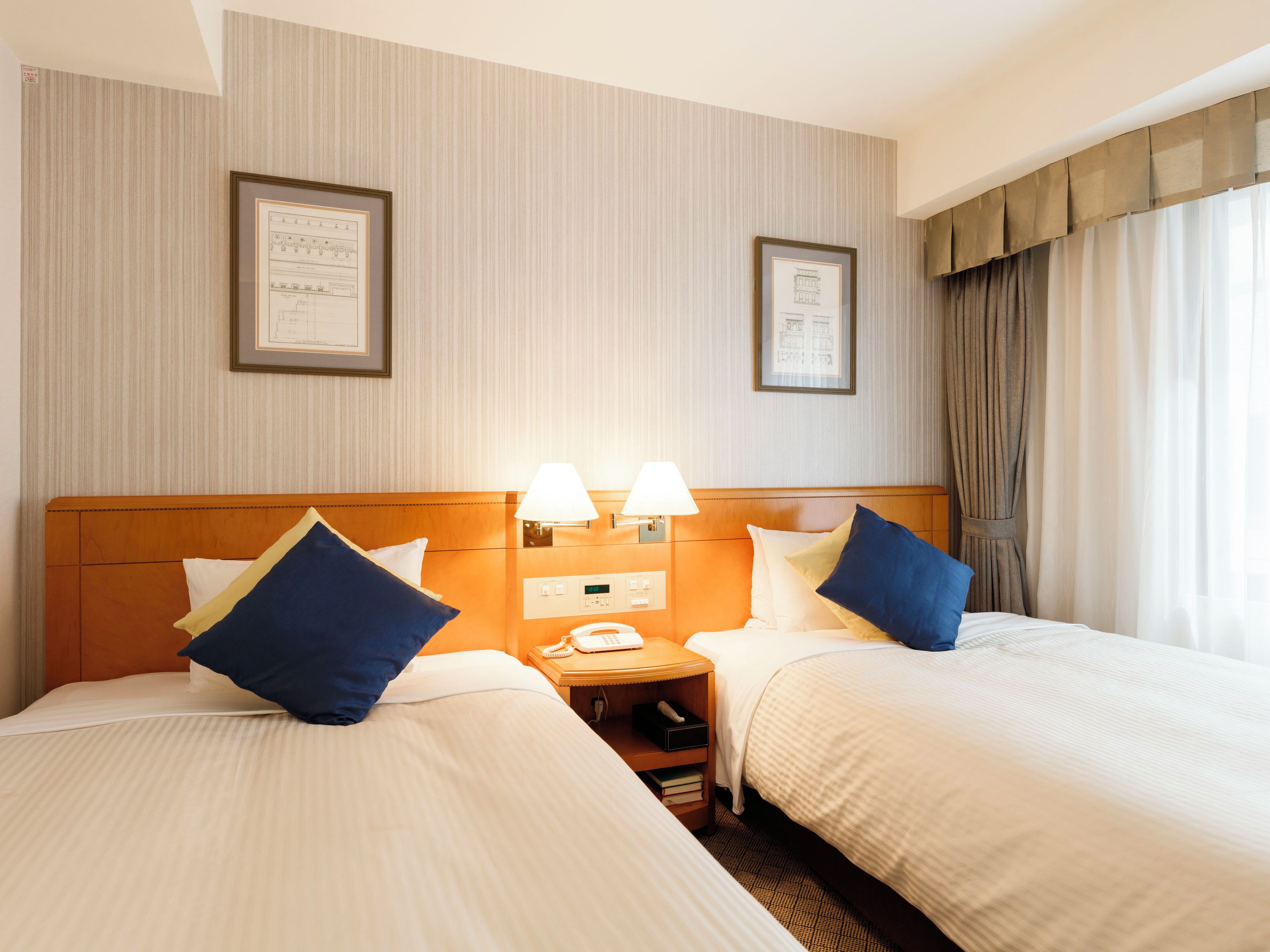 A hotel room with two beds, a nightstand with a phone, and framed pictures on the wall.