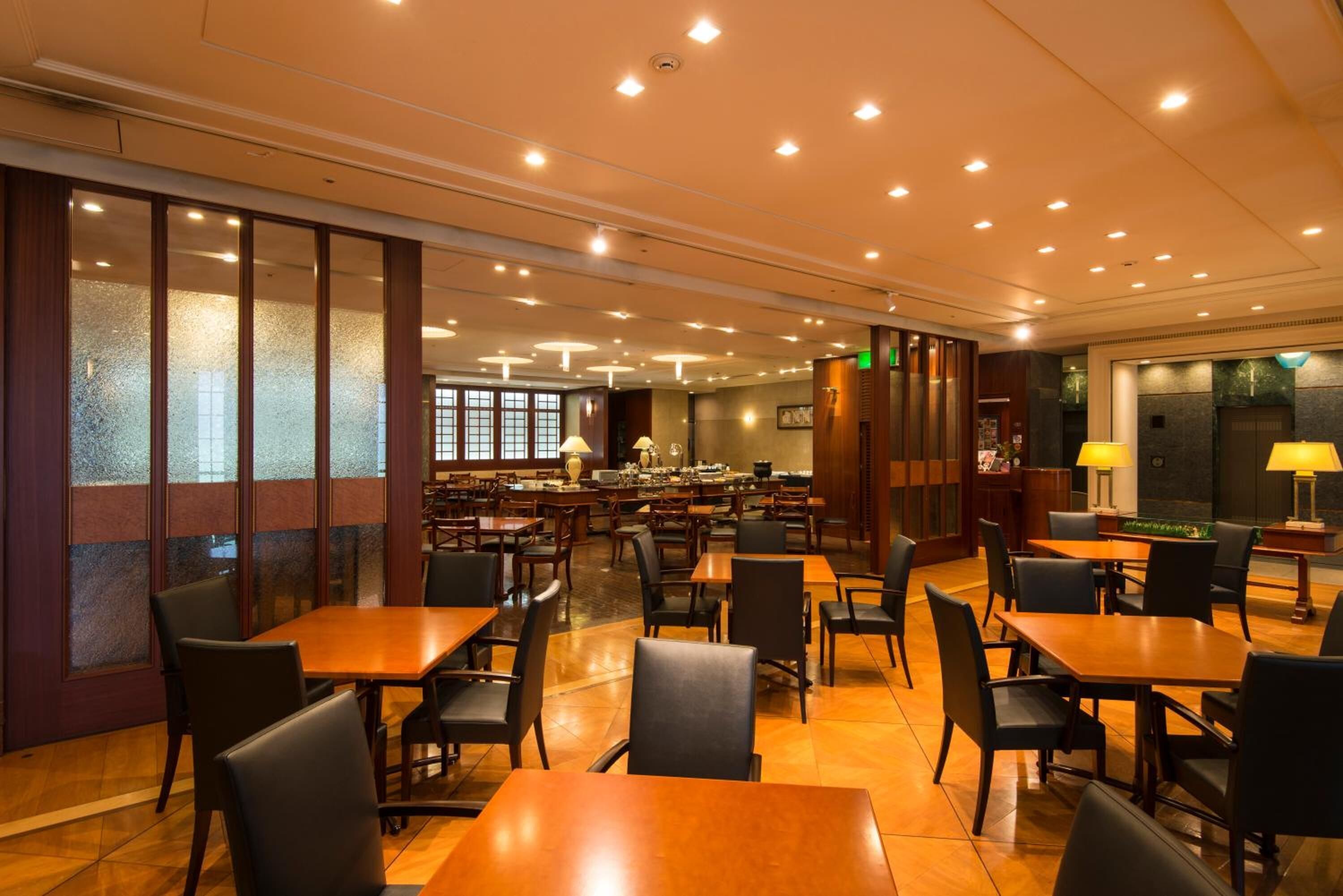 A spacious restaurant with multiple tables and chairs, a bar area, and a view of the kitchen in the background.