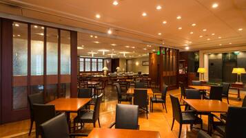 A spacious restaurant with multiple tables and chairs, a bar area, and a view of the kitchen in the background.