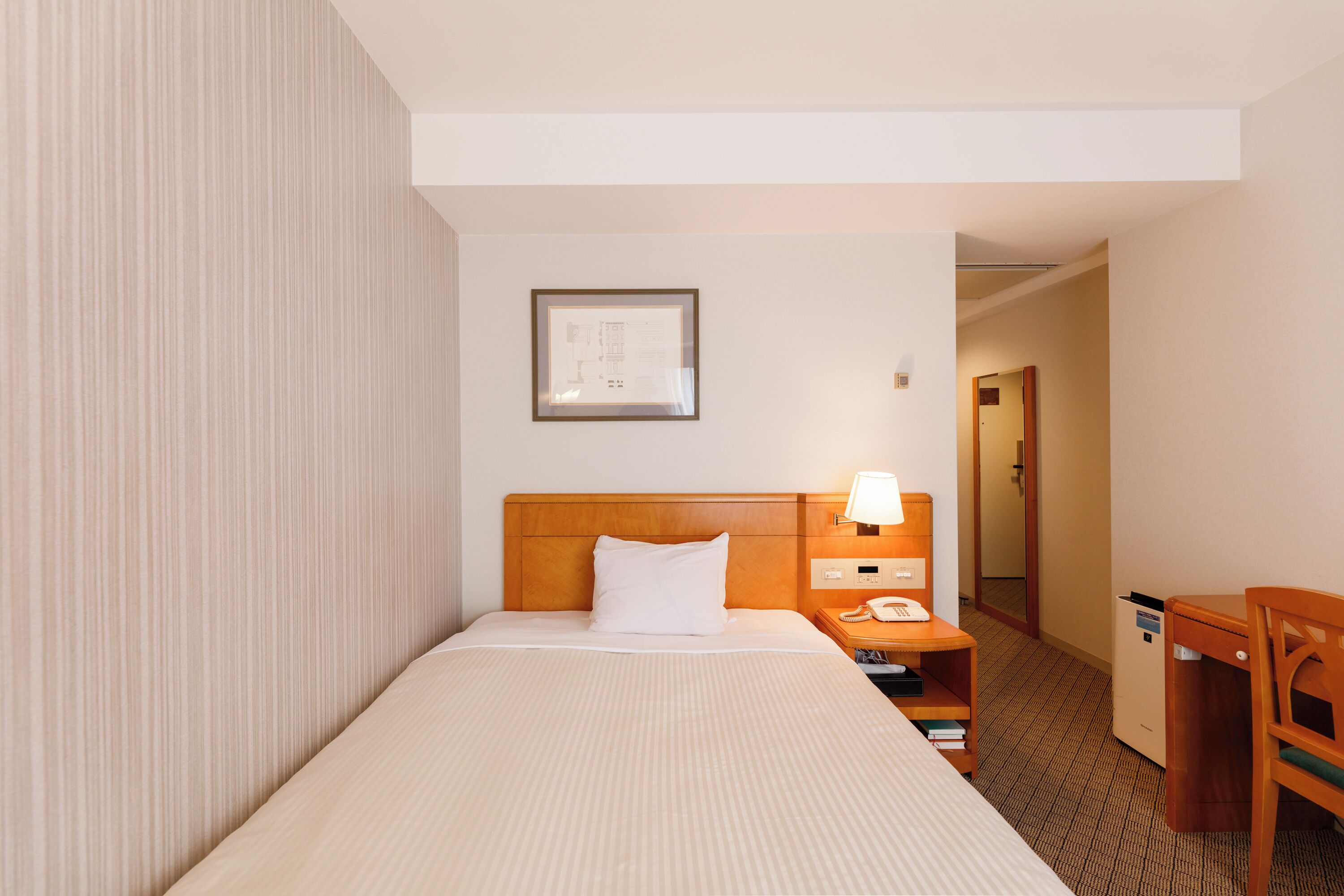 A hotel room with a bed, bedside table, lamp, and a framed picture on the wall.