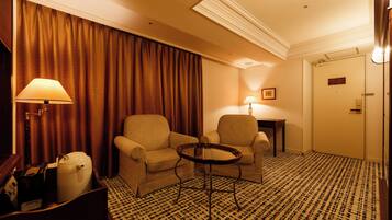 Habitación de hotel con dos sillones, una mesita, una lámpara, un cesto de basura y una alfombra estampada.