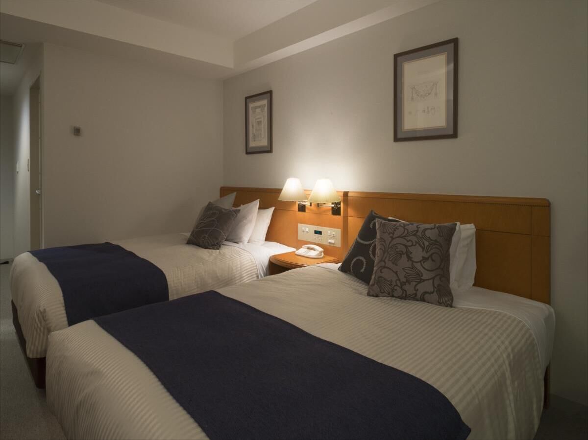 A hotel room with two beds, a nightstand with a lamp, and framed pictures on the wall.