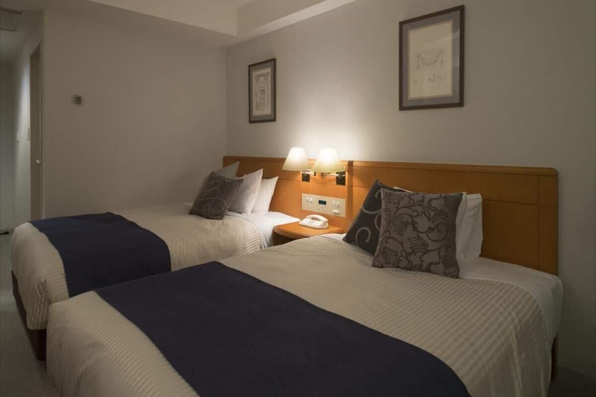 A hotel room with two beds, a nightstand with a lamp, and framed pictures on the wall.