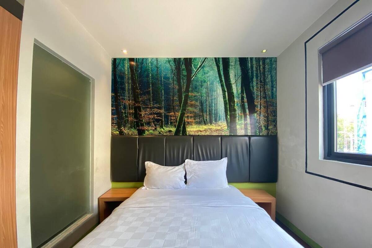Un dormitorio con una cama grande, cabecera, mesita de noche, ventana y pared con un mural de un bosque.
