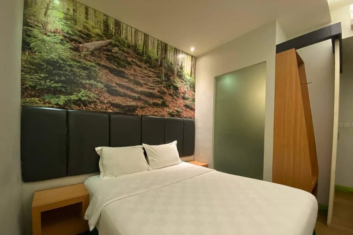 Una habitación de hotel moderna con una cama grande, cabecera con un mural de bosque, una mesita de noche de madera y una puerta de madera.