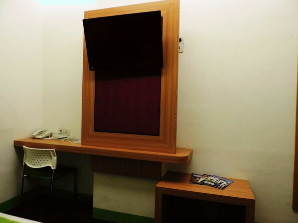 A small room with a wooden desk, a chair, a small table with magazines, and a window with a dark curtain.