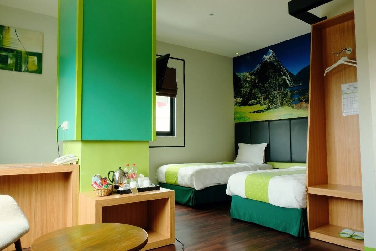 Una habitación de hotel con dos camas, un escritorio, una silla y un cuadro de un paisaje montañoso.