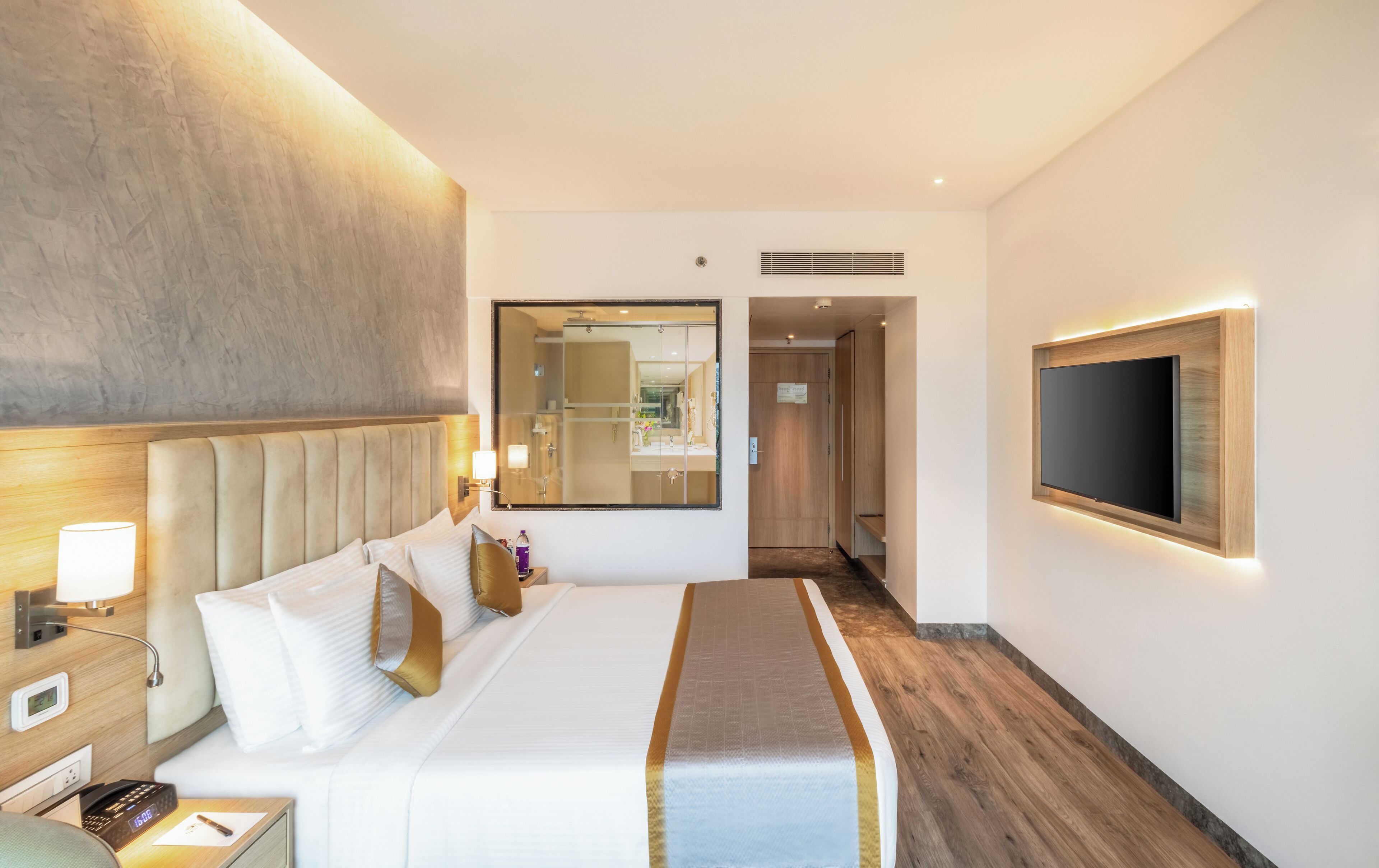 A hotel room with a large bed, bedside tables, a TV, a mirror, and a wooden floor.