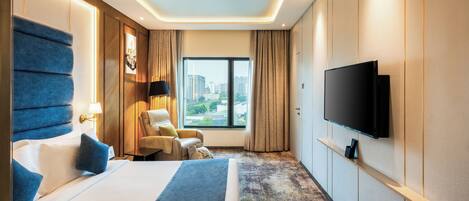 Habitación de hotel con una cama grande, un escritorio, una silla, un televisor montado en la pared y una ventana con vistas a la ciudad.