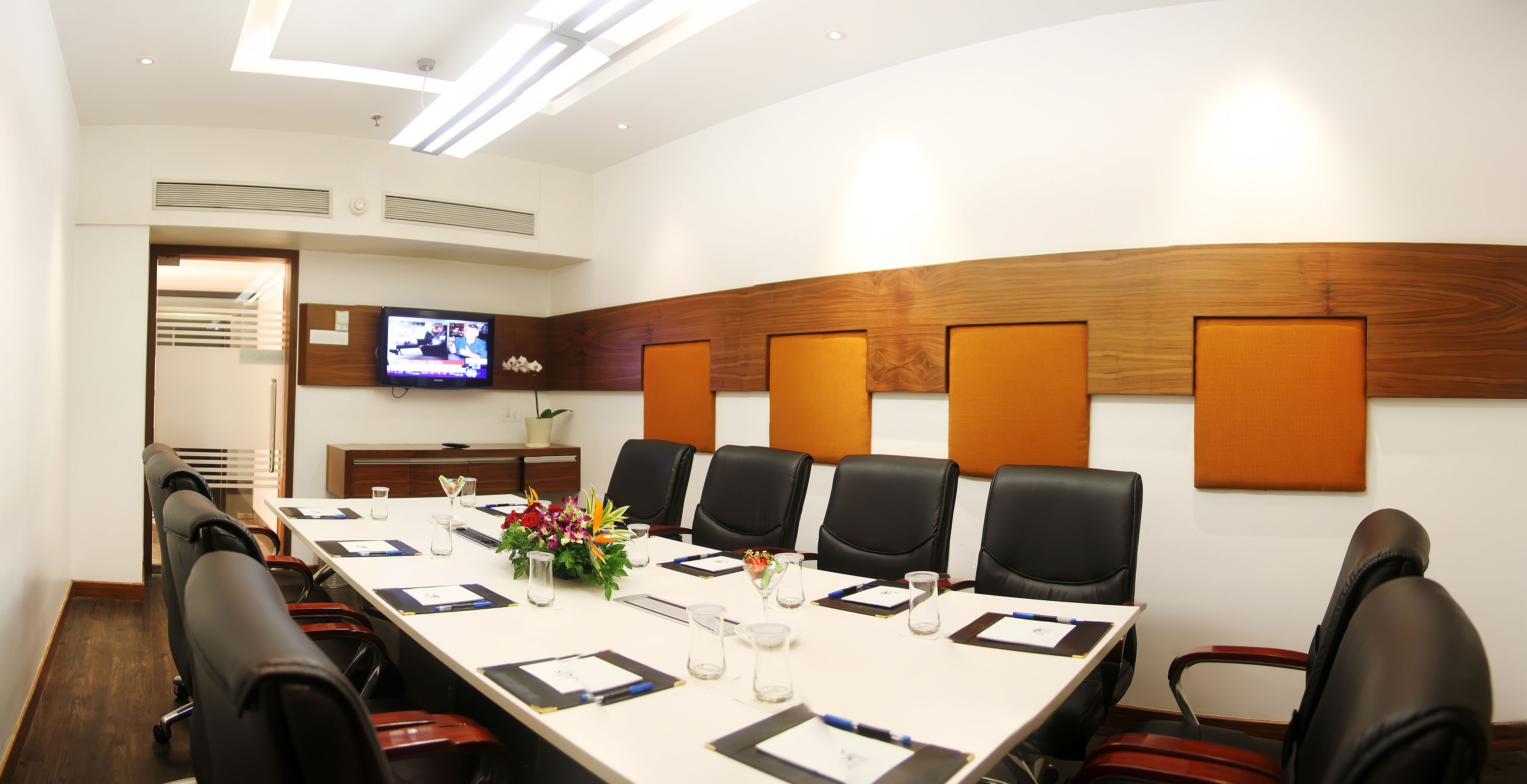 A conference room with a long table, black chairs, and a television on the wall.