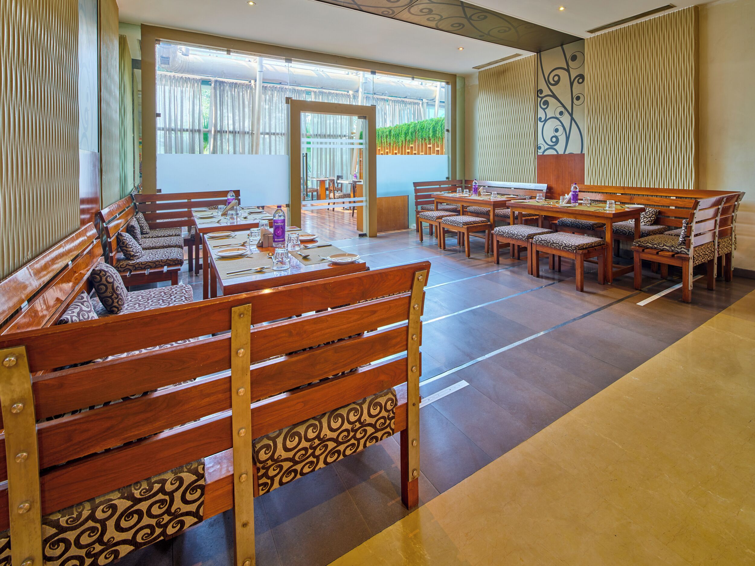 A spacious dining area with wooden benches and tables, large windows with curtains, and a view of the outdoors.