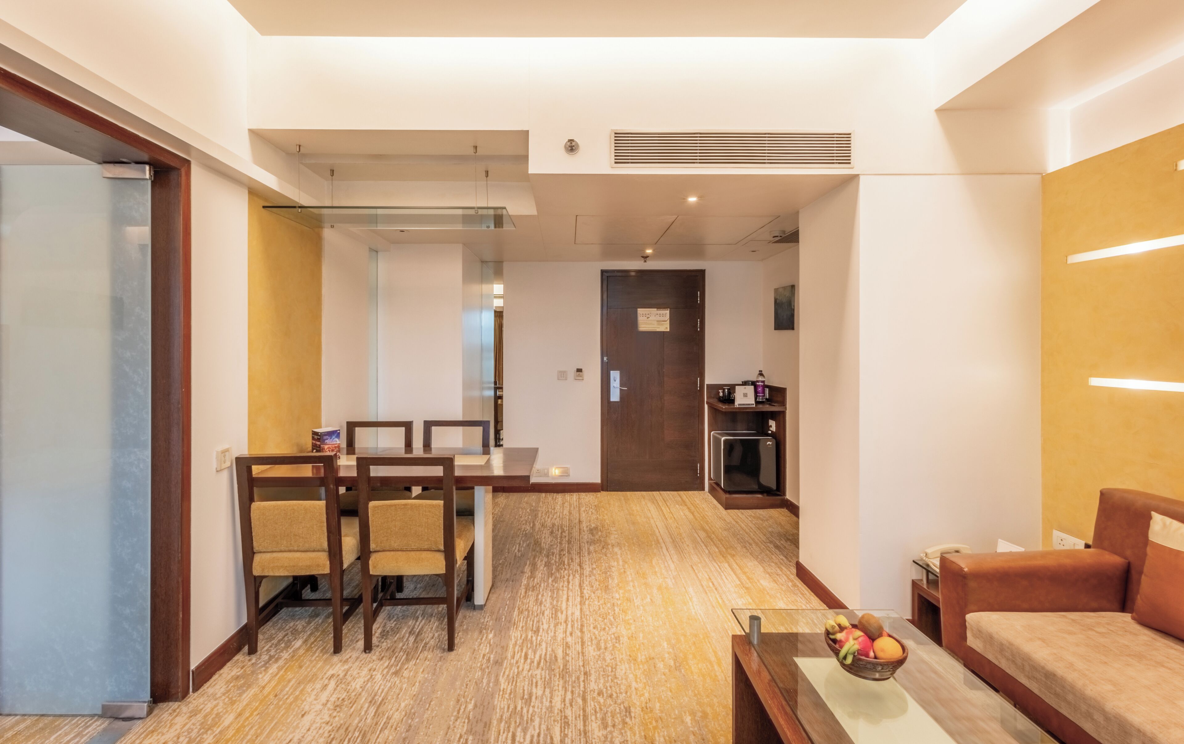A hotel room with a dining area, a kitchenette, and a seating area with a fruit bowl.