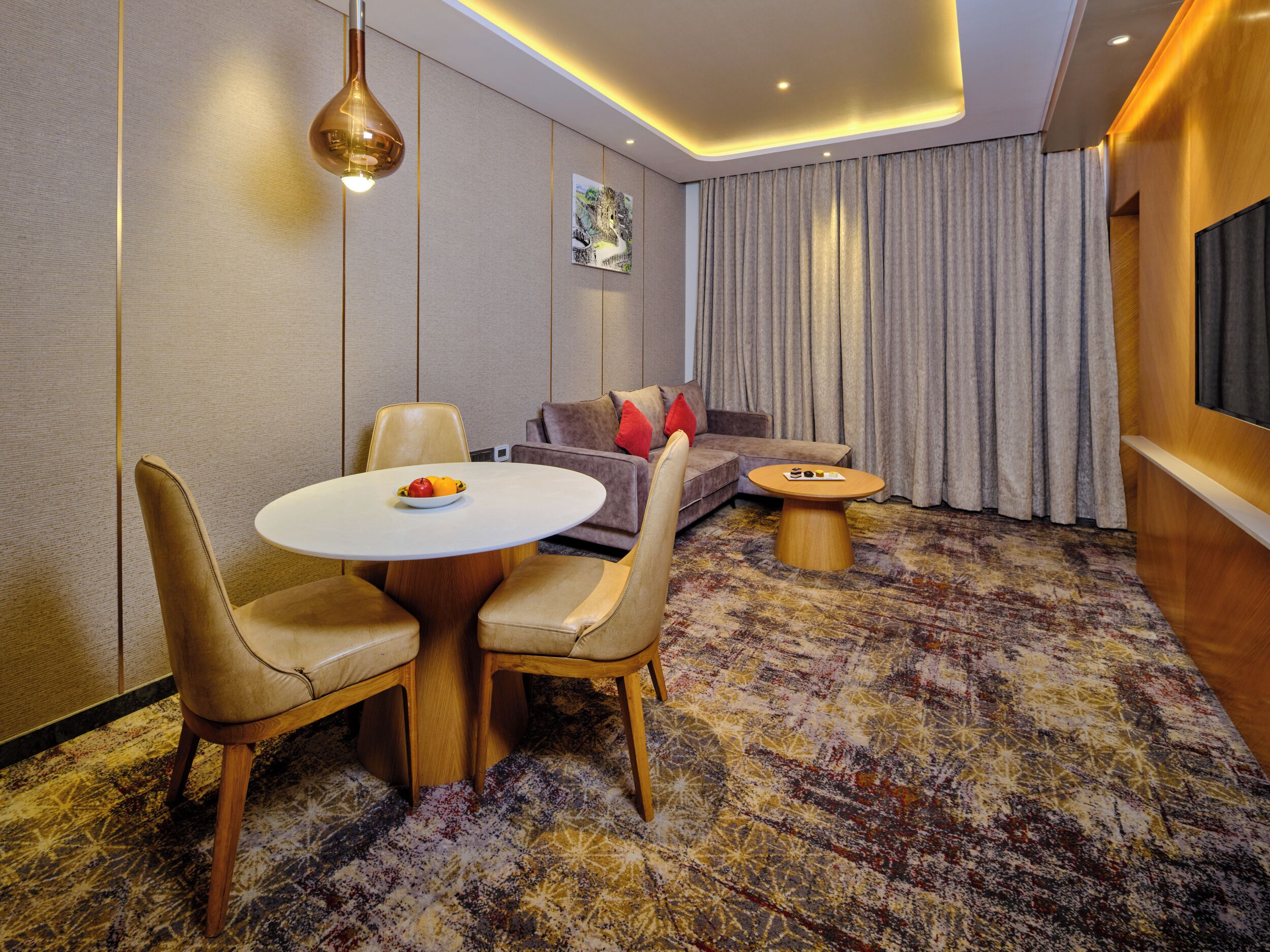 A modern hotel room with a dining area, a sofa, and a TV.