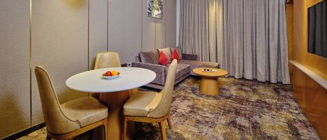 Una habitación de hotel moderna con zona de comedor, sofá y televisor.