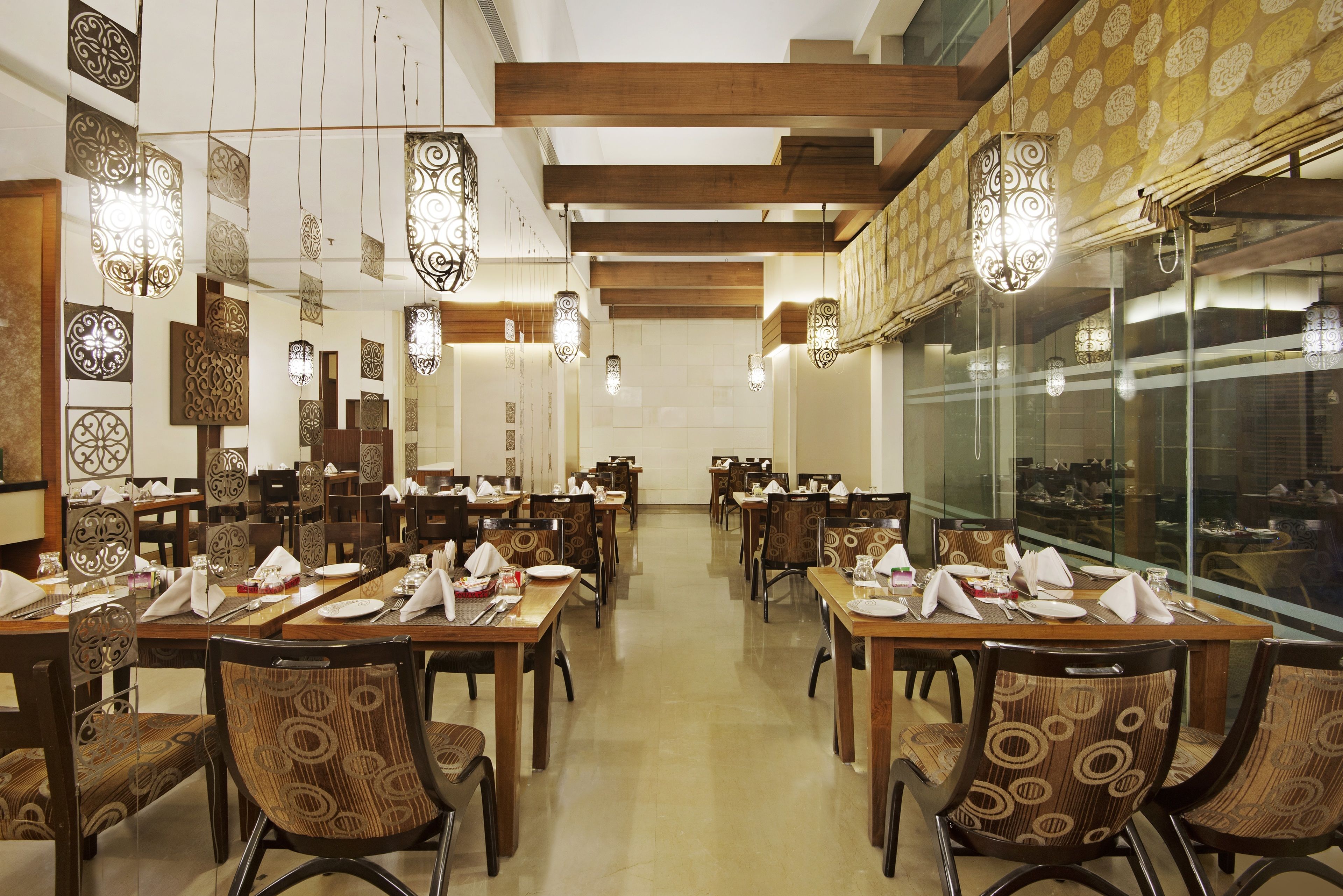A restaurant with multiple dining tables and chairs, patterned wall decor, and hanging light fixtures.
