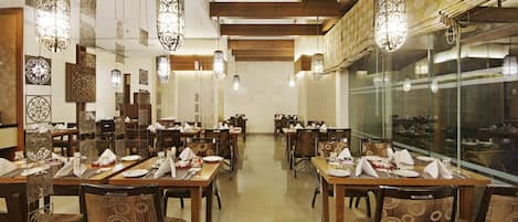 A restaurant with multiple dining tables and chairs, patterned wall decor, and hanging light fixtures.