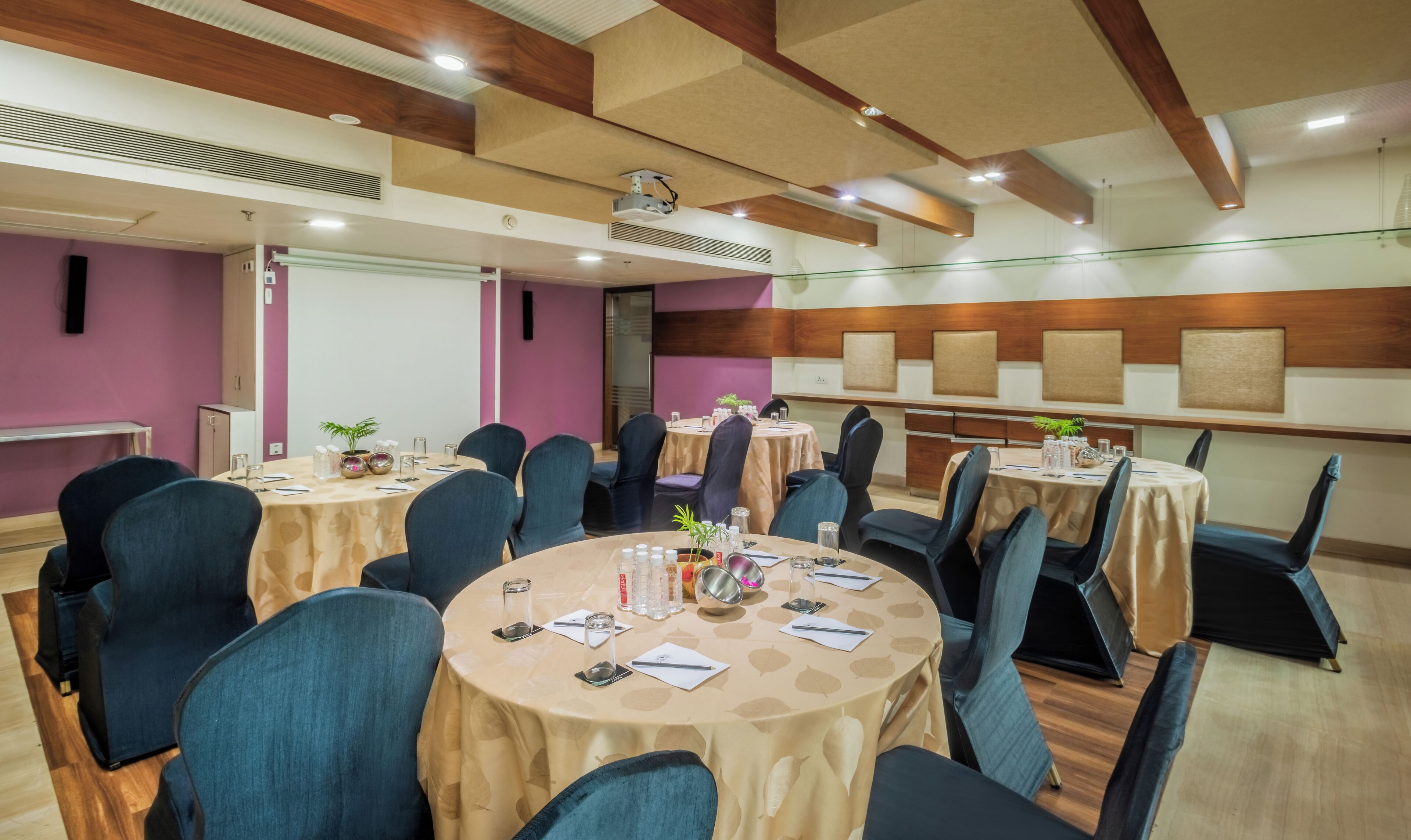 Een congreszaal met ronde tafels, stoelen en een beamer.