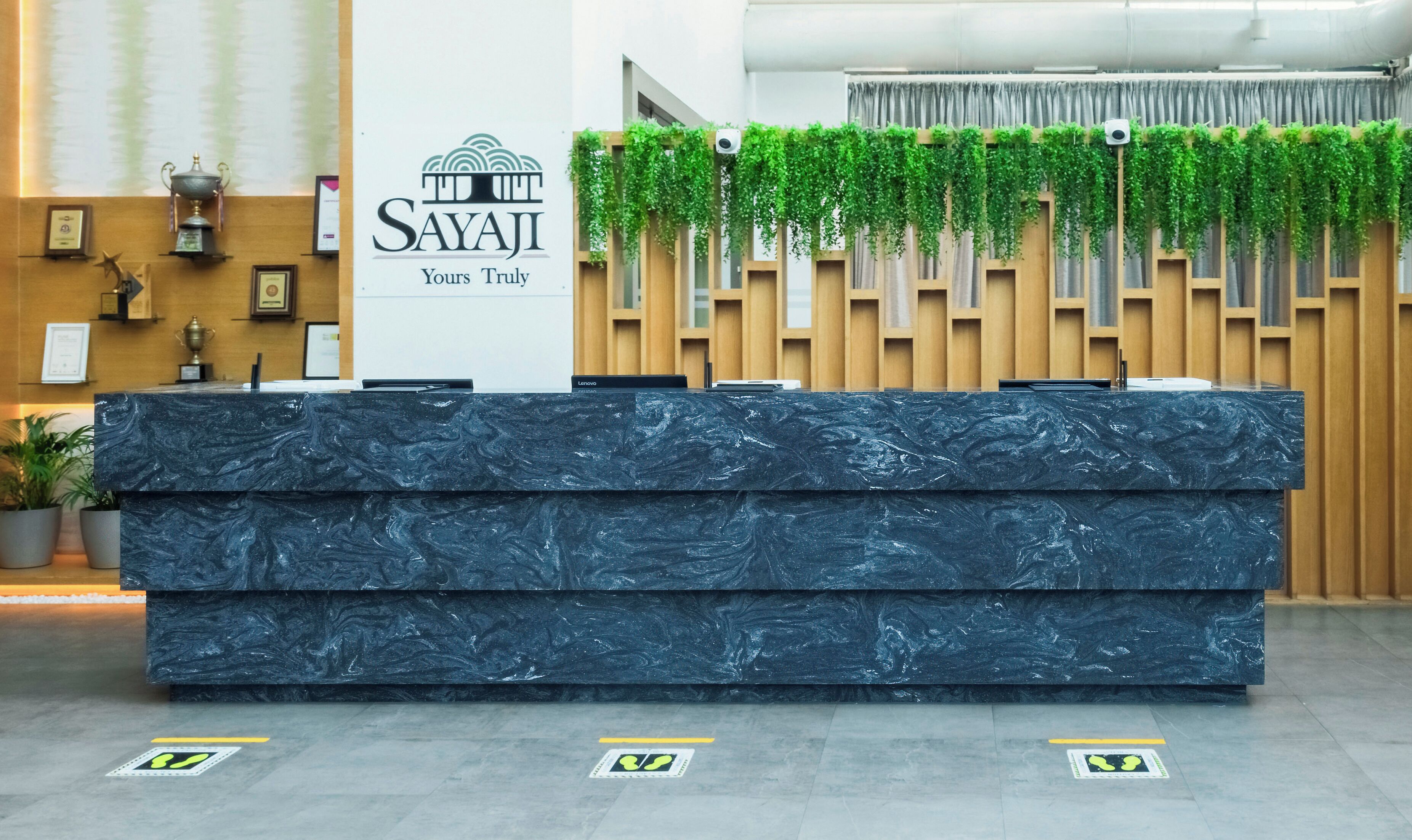 A reception desk with a logo, a plant-covered wall, and a trophy on the wall.
