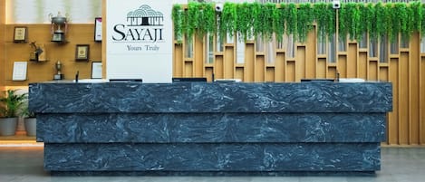 A reception desk with a logo, a plant-covered wall, and a trophy on the wall.