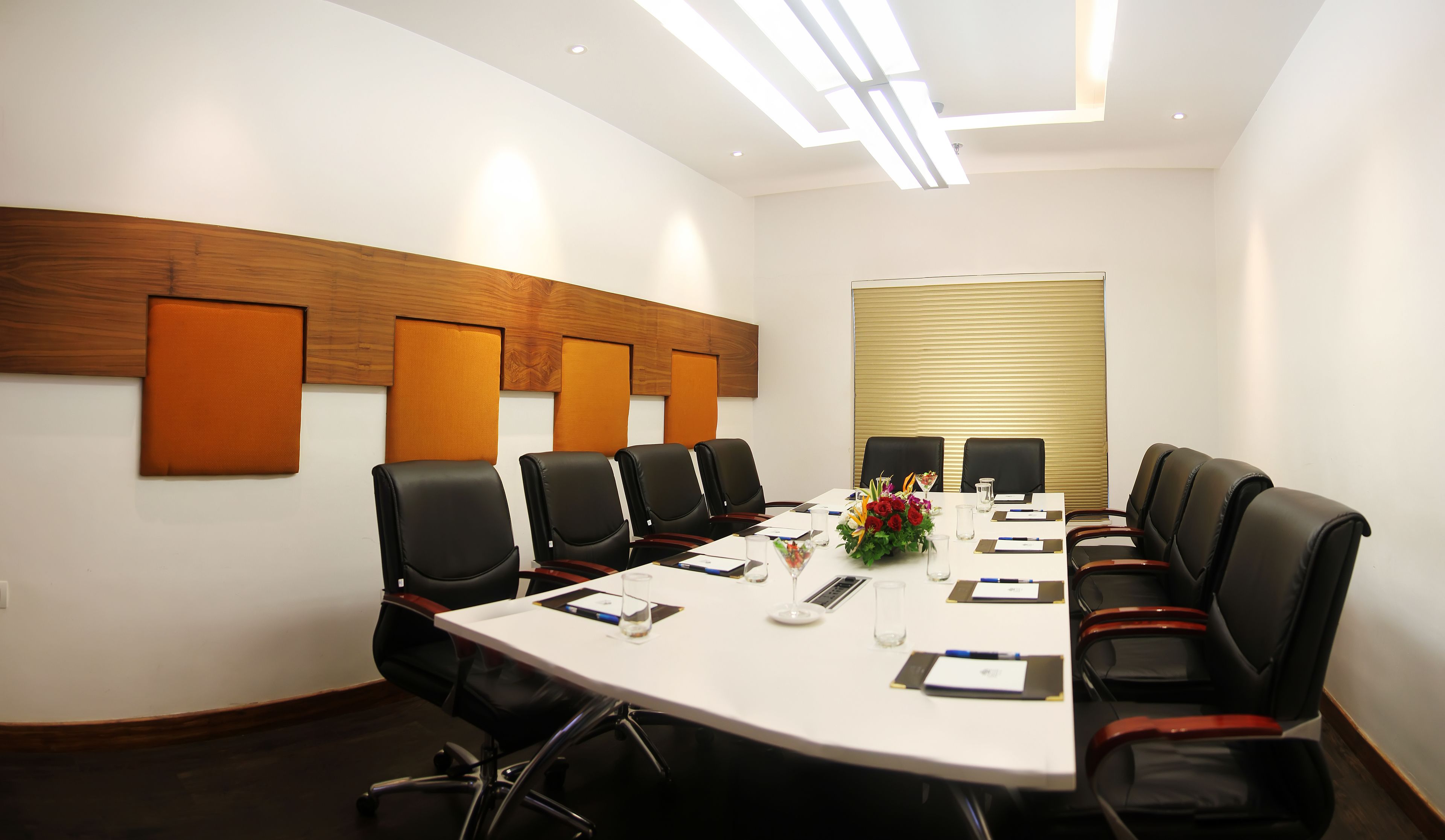 A conference room with a white table, black chairs, and a wooden accent wall.