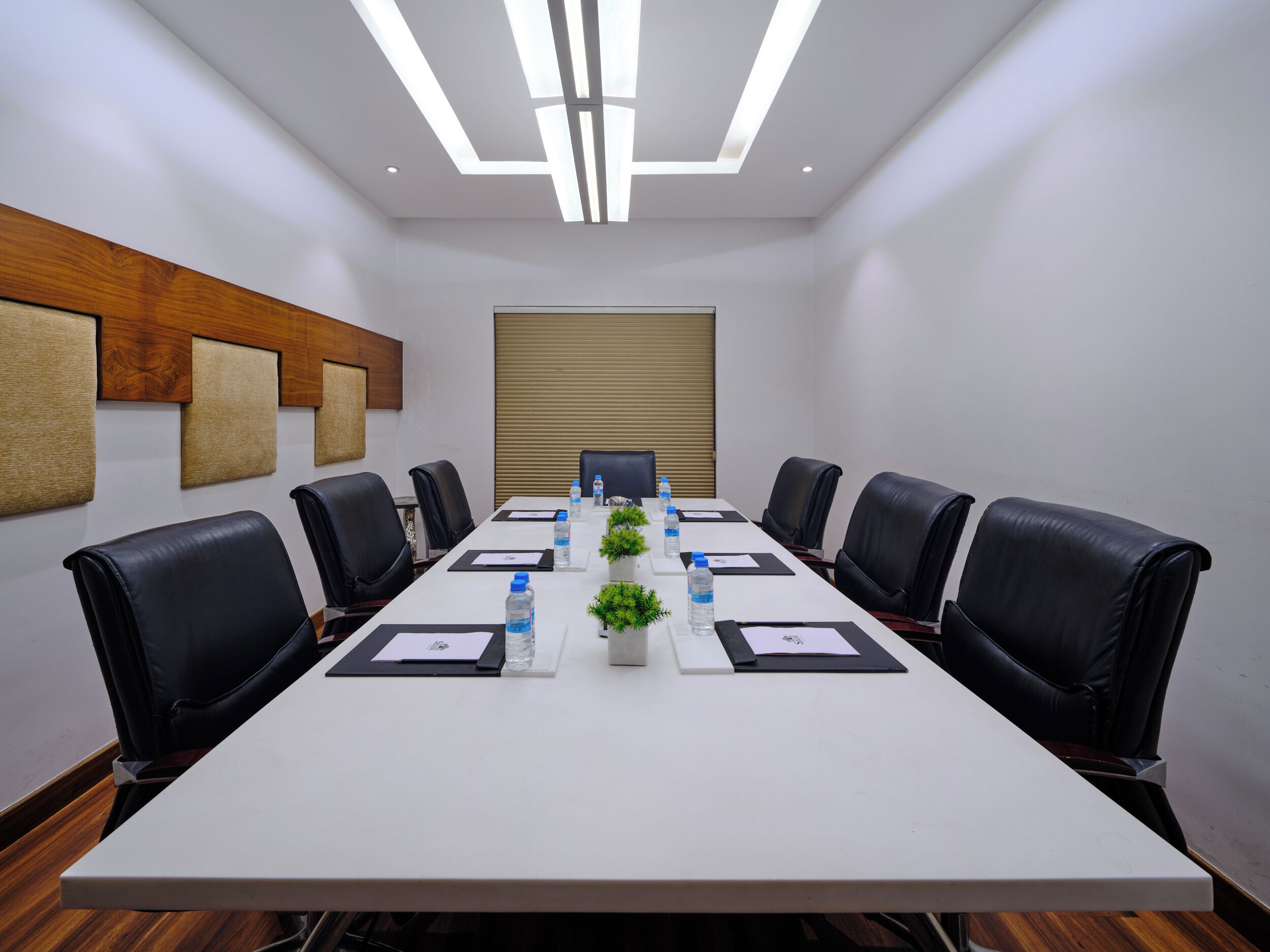 A conference room with a long table, black leather chairs, water bottles, and a potted plant.