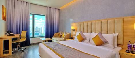A hotel room with a large bed, a desk with a chair, a sofa, and a view of the city.