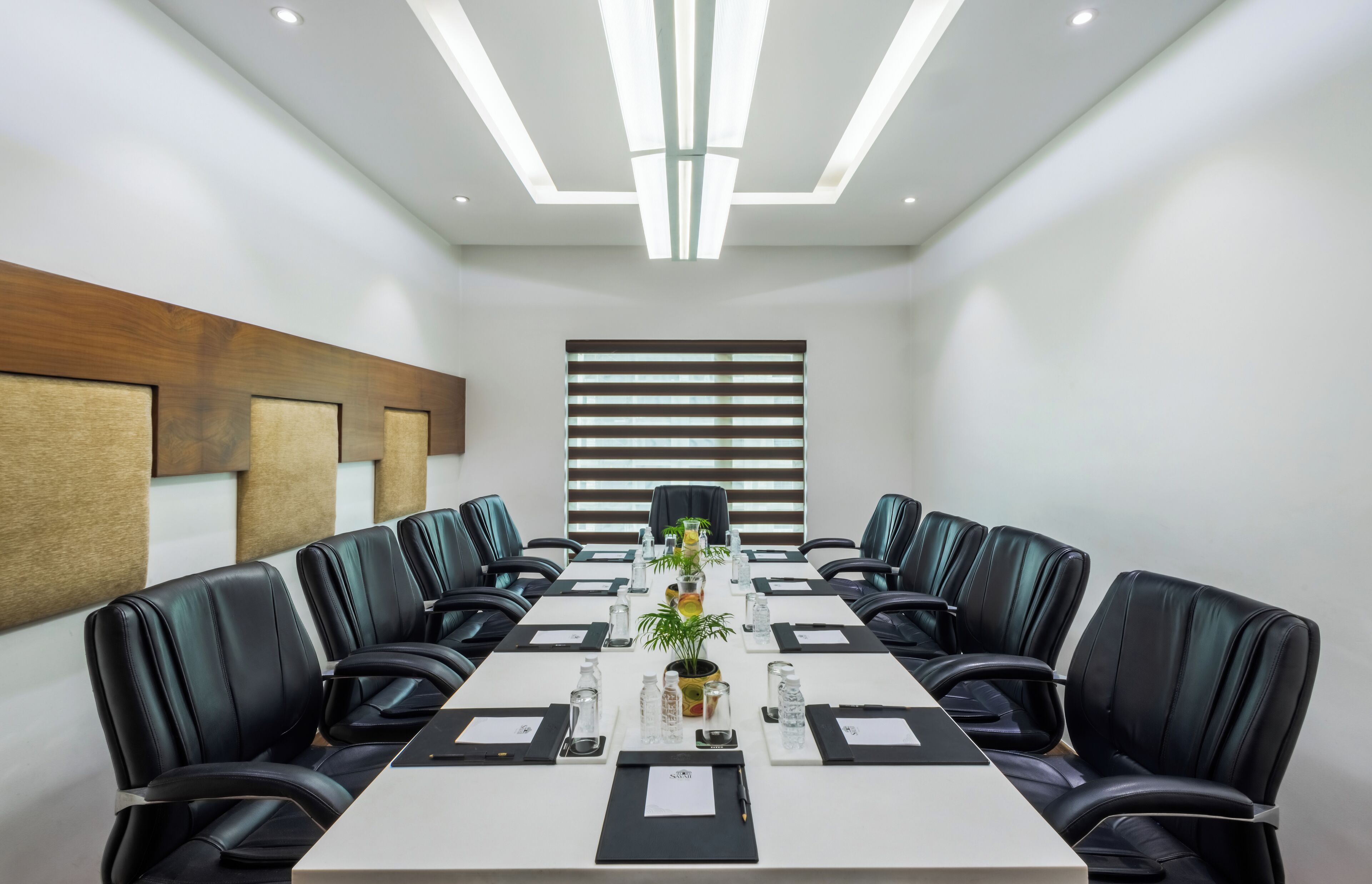 A conference room with a long table, black leather chairs, and a modern ceiling design.