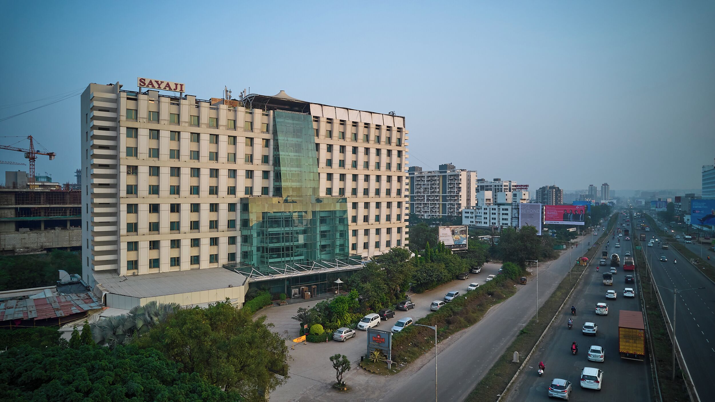 A multi-story hotel with a modern facade, a prominent sign, and a parking area with several vehicles.