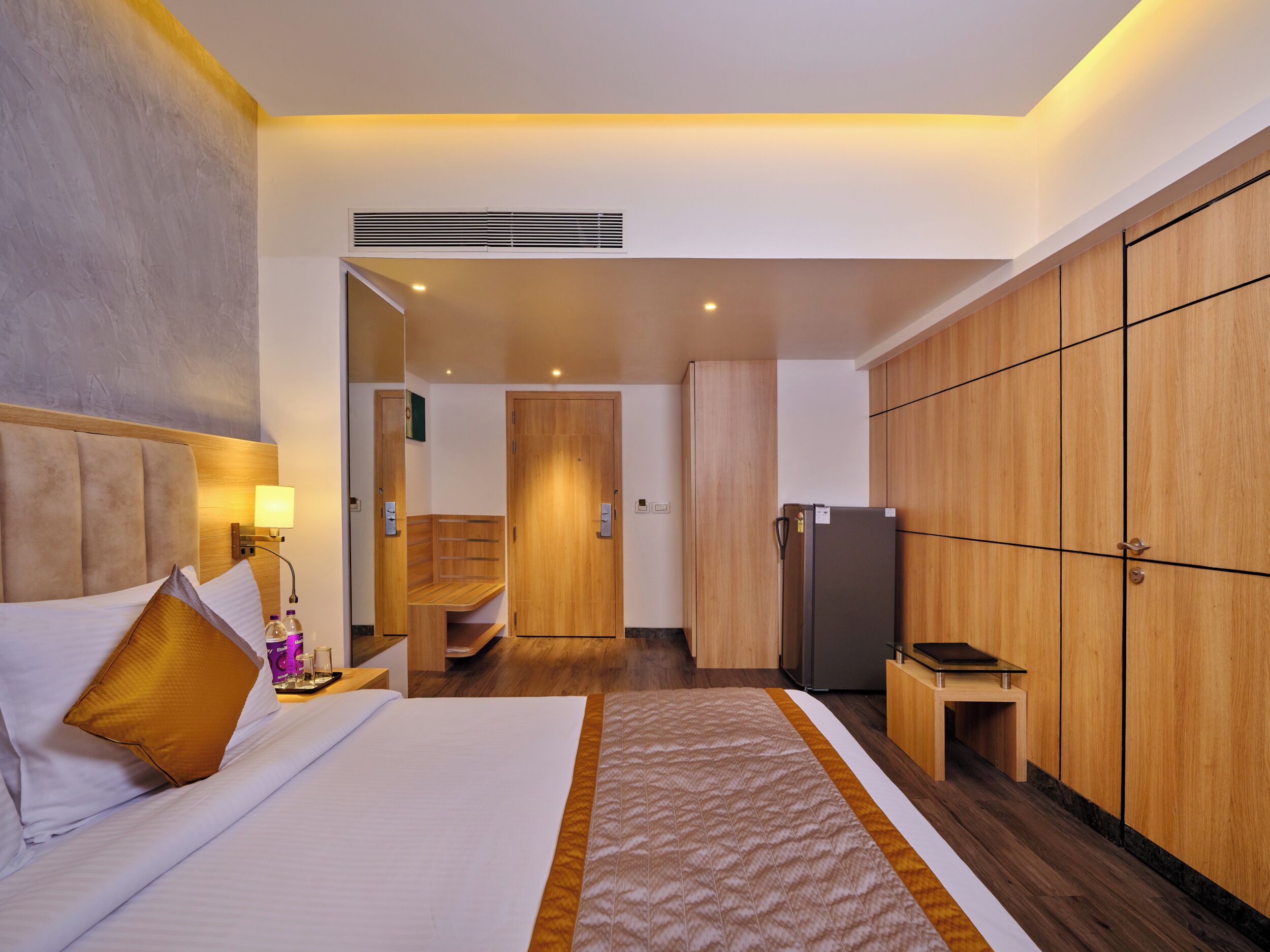 A hotel room with a bed, a wardrobe, a refrigerator, and a bathroom visible through an open door.