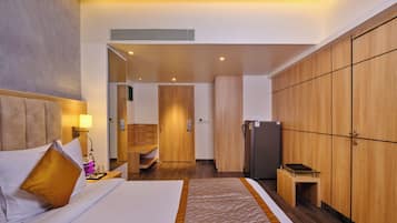 Habitación de hotel con cama, armario, refrigerador y baño visible a través de una puerta abierta.